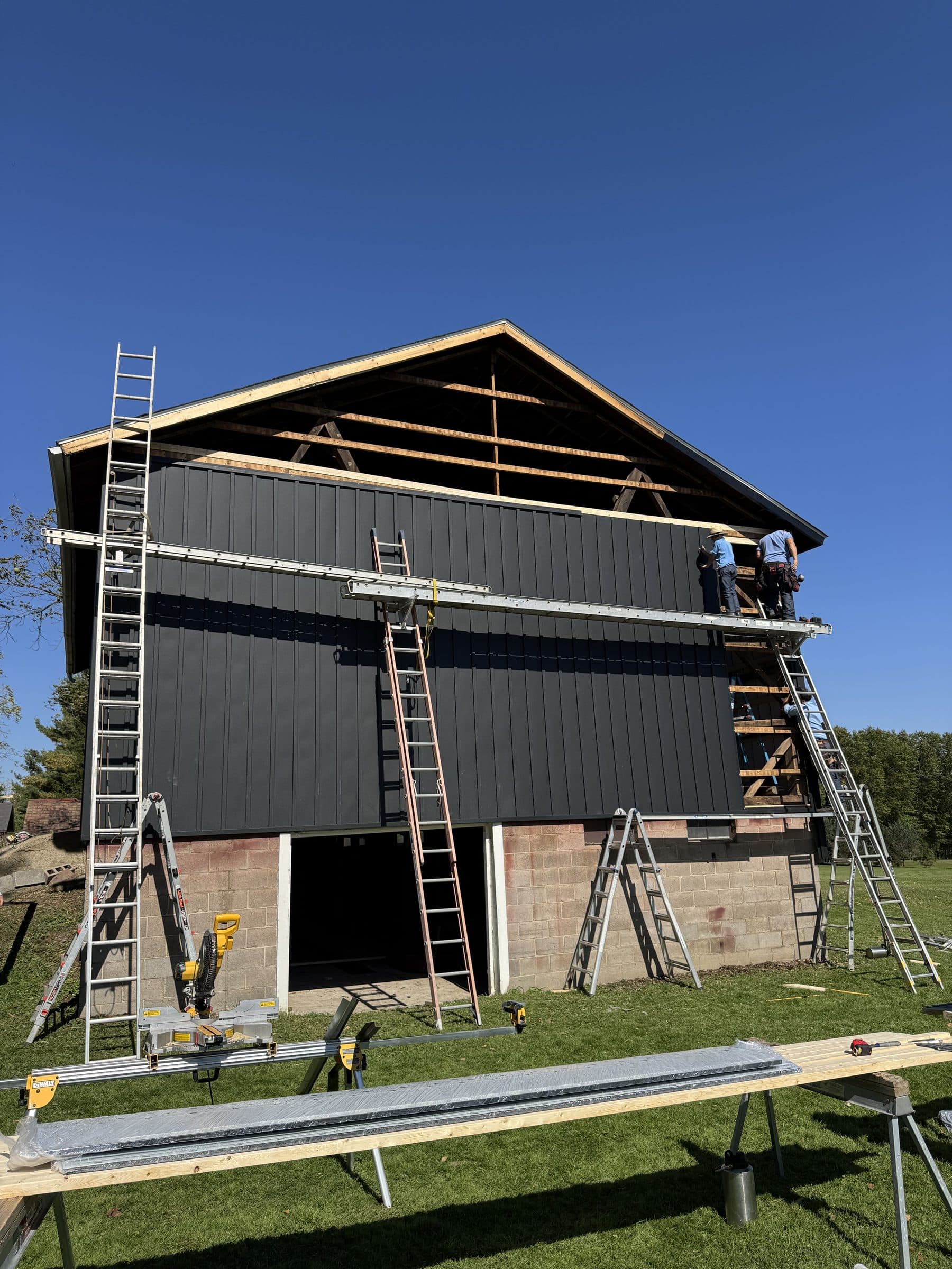 Workers installing black metal siding on the barn gable