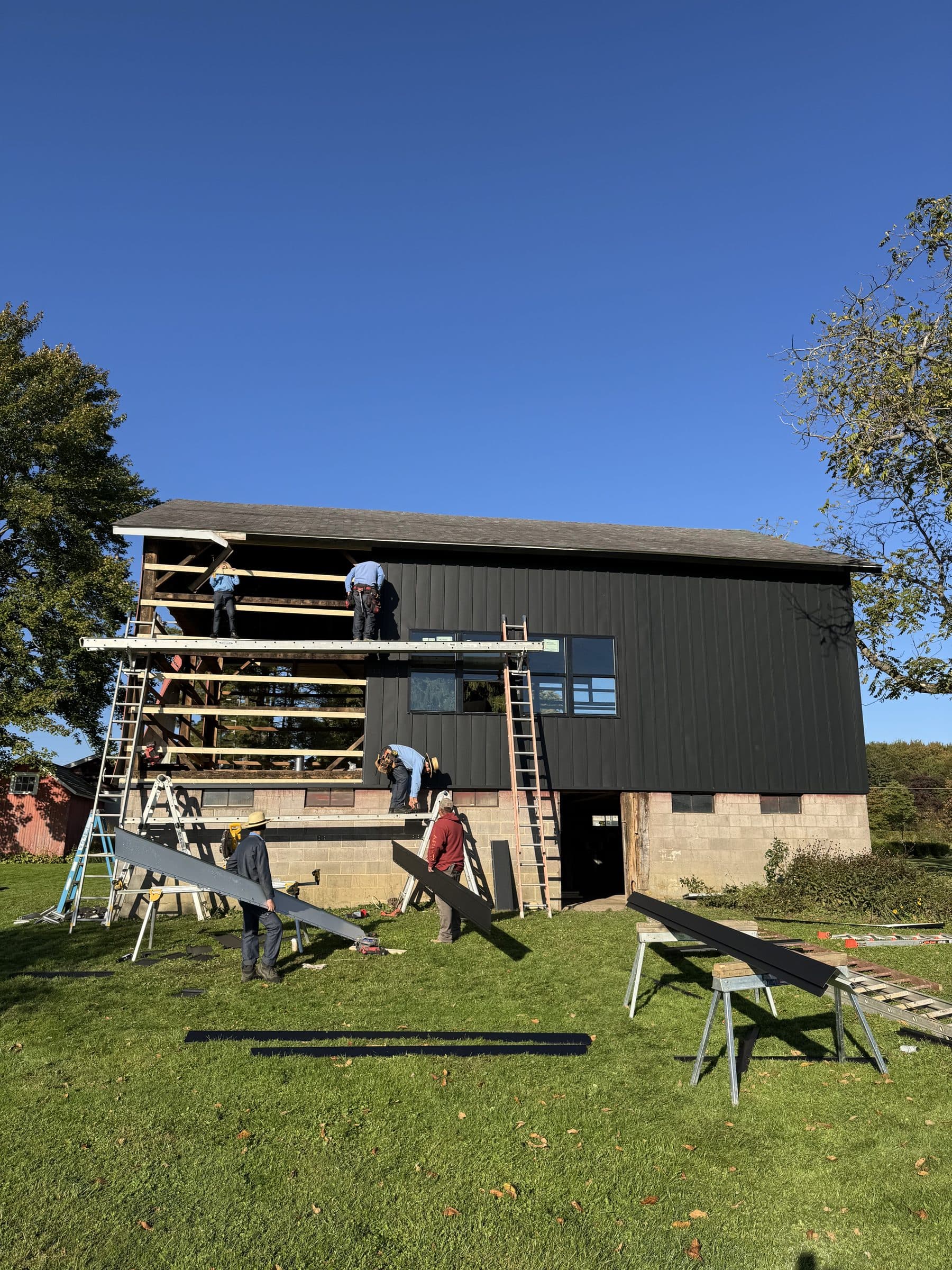 Crew installing black metal siding on the barn side wall